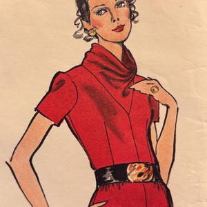 Op de afbeelding: Illustratie van een vrouw in een rode jurk met een zwarte riem en een gouden gesp. De jurk heeft korte mouwen en een hoge halslijn. De vrouw draagt gouden oorbellen, een ring en een armband. Haar haar is opgestoken.