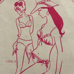 May include: Pink line drawing of two figures in swimwear. One figure wears a wide-brimmed hat and a bikini with bows. The other figure wears sunglasses and a bikini. Text reads "VIEW B" and "VIEW A".
