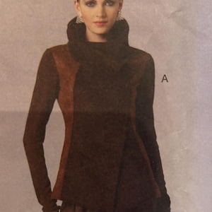 May include: A brown and tan long-sleeved top with a high cowl neck and a wrap-style front. The top is made of a soft, textured fabric.