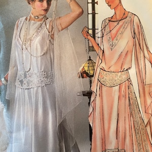 May include: Two women wearing vintage-style dresses with long beaded necklaces. The dress on the left is white with a lace overlay and a sheer cape. The dress on the right is pink with a floral pattern and a beaded belt.