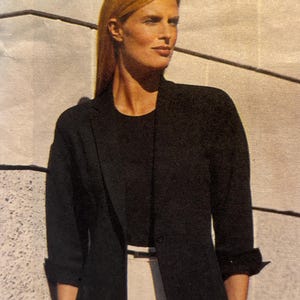 May include: A black blazer with a single button closure and three-quarter length sleeves, worn over a black top and light-colored trousers. The blazer features a notched lapel and a textured fabric finish, providing a structured appearance.