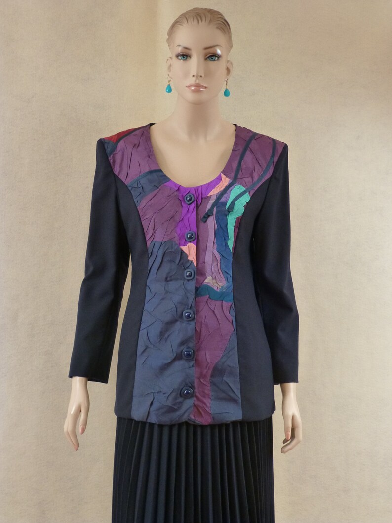 May include: A black blazer with a purple, blue and green abstract patterned panel on the front. The blazer has a button closure and long sleeves.