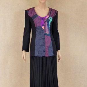 May include: A black blazer with a colourful abstract pattern on the front. The blazer has a scoop neckline and a button closure. The blazer is paired with a black pleated skirt.
