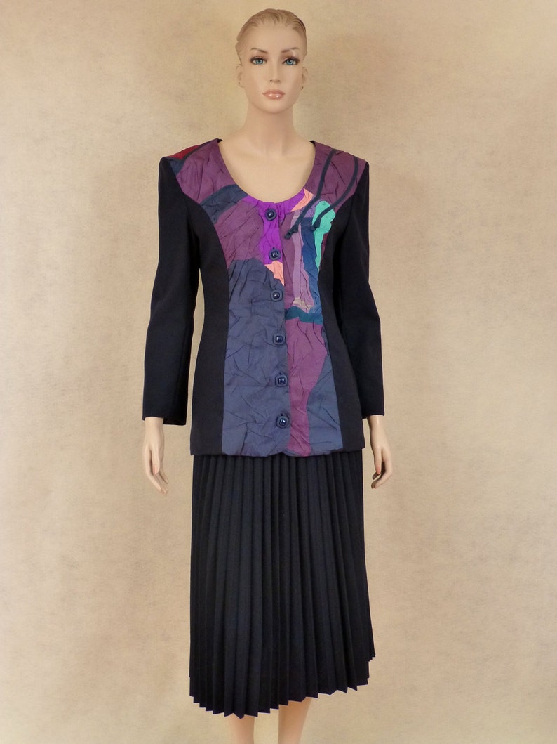 May include: A black blazer with a colourful abstract pattern on the front. The blazer has a scoop neckline and a button closure. The blazer is paired with a black pleated skirt.