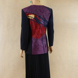 May include: A black blazer with a purple, red and yellow abstract design on the back. The blazer is paired with a black pleated skirt.