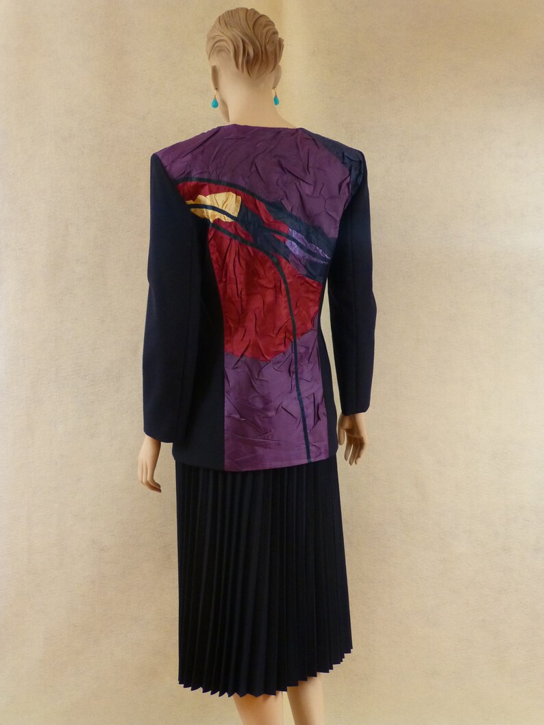 May include: A black blazer with a purple, red and yellow abstract design on the back. The blazer is paired with a black pleated skirt.