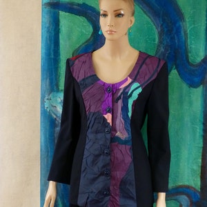 May include: A black blazer with a colourful abstract print on the front. The print features shades of purple, pink, blue, and green. The blazer has a button-up closure and long sleeves.