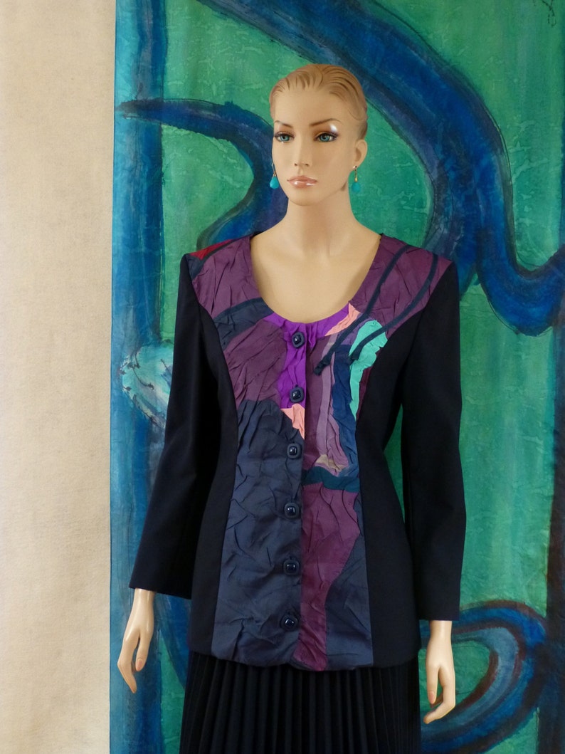May include: A black blazer with a colourful abstract print on the front. The print features shades of purple, pink, blue, and green. The blazer has a button-up closure and long sleeves.