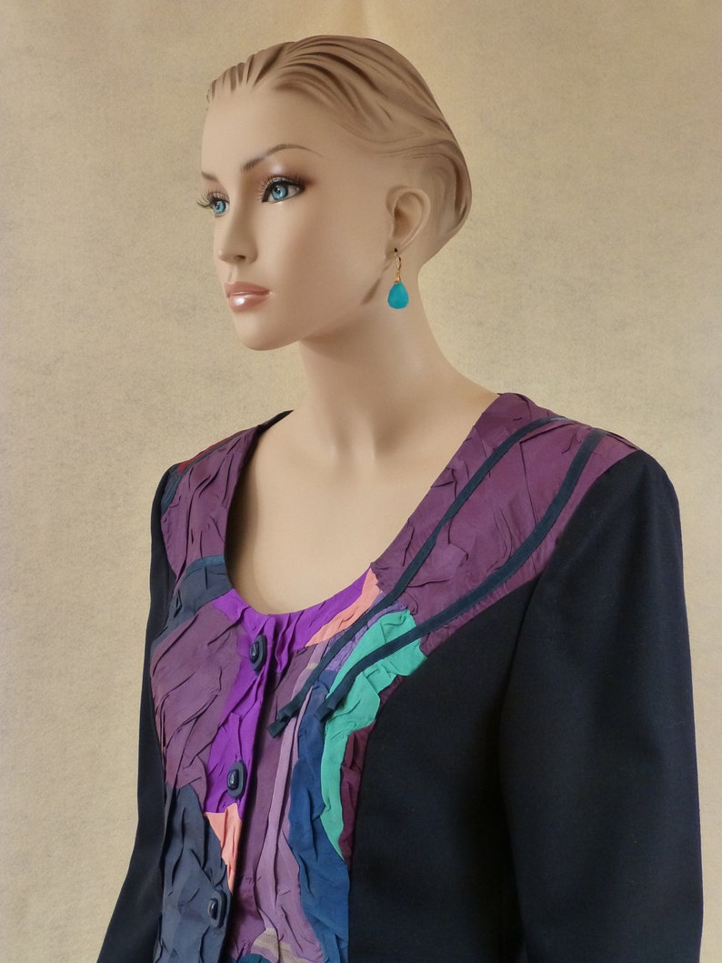 May include: A black blazer with a colourful, abstract patterned panel on the front. The panel features shades of purple, pink, green, and grey. The blazer has a button closure and long sleeves.