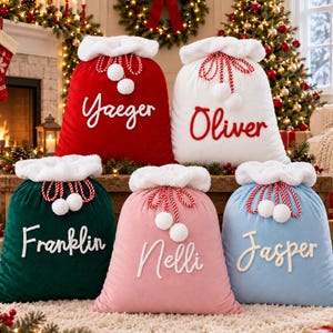 Pode incluir: Cinco sacos de presente de Natal de pelúcia com punhos de pele sintética branca e cordões trançados vermelhos e brancos com pompons. O saco vermelho diz Yaeger, o branco Oliver, o verde Franklin, o rosa Nelli e o azul Jasper.