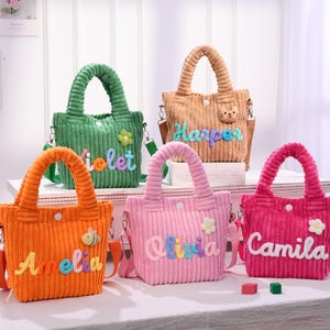 Puede incluir: Cinco bolsos tote de pana en varios colores: naranja, verde, beige, rosa y fucsia. Cada bolso presenta un nombre bordado en letras coloridas. Los bolsos tienen asas a juego y correas ajustables. Elementos decorativos: una flor y una abeja.