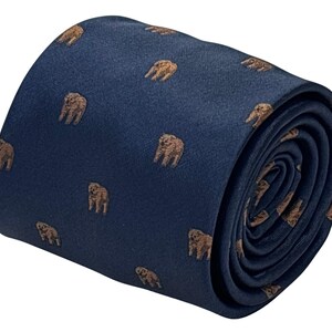 Puede incluir: Corbata enrollada azul marino con un patrón repetido de pequeñas figuras de elefantes marrones. La corbata está hecha de una tela suave y enrollada, mostrando el patrón y la textura.