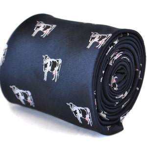May include: Rolled navy blue tie with a repeating pattern of cartoon cows. The cows are white with black spots and pink udders. The tie is made of a smooth material, possibly silk.