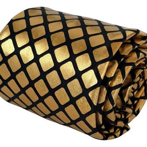 May include: A rolled necktie featuring a metallic gold grid pattern set against a solid black background. The fabric displays a repeating geometric square design with rounded corners, creating a textured appearance across the entire surface.