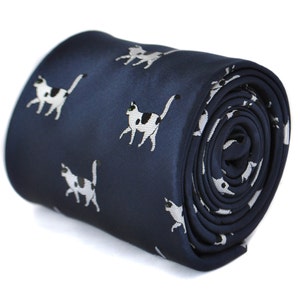 Puede incluir: Una corbata de seda azul marino con un patrón repetido de gatos blancos y negros. La corbata está enrollada y lista para ser usada.