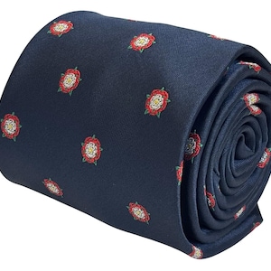 May include: Rolled navy blue tie featuring a repeating pattern of red and white Tudor roses. The tie is made of a smooth fabric and is tightly rolled, showcasing the floral design. A classic accessory for formal or semi-formal occasions.