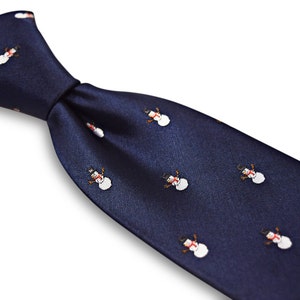 Puede incluir: Una corbata de seda azul marino con un patr&oacute;n repetido de mu&ntilde;ecos de nieve blancos. Los mu&ntilde;ecos de nieve tienen sombreros negros, narices naranjas y ojos negros.