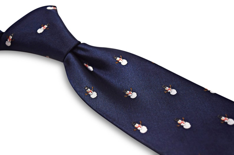 Puede incluir: Una corbata de seda azul marino con un patr&oacute;n repetido de mu&ntilde;ecos de nieve blancos. Los mu&ntilde;ecos de nieve tienen sombreros negros, narices naranjas y ojos negros.