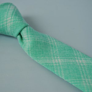 May include: A green and white plaid tie. The tie is made of a soft, textured fabric.