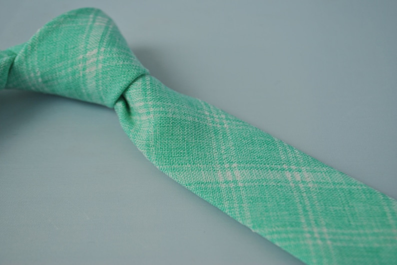 May include: A green and white plaid tie. The tie is made of a soft, textured fabric.