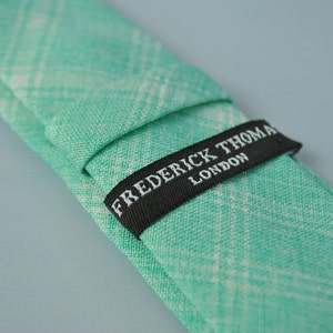 May include: A green and white plaid tie with a black label that reads "FREDERICK THOMAS LONDON".