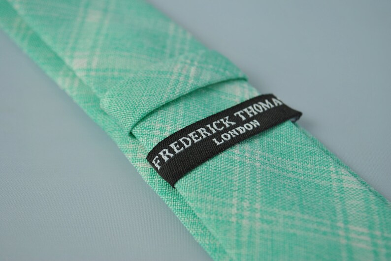 May include: A green and white plaid tie with a black label that reads "FREDERICK THOMAS LONDON".