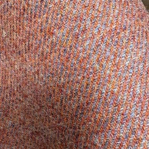 May include: A close-up view of a woven textile featuring a diagonal twill pattern. The fabric is composed of alternating threads in vibrant orange and soft lavender, creating a textured, multi-colored appearance with a visible fiber structure.