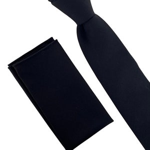 Könnte beinhalten: Ein schwarzes Krawatten- und Einstecktuch-Set. Die Krawatte ist aus glattem Stoff gefertigt und hat ein klassisches Design. Das Einstecktuch ist ebenfalls aus glattem Stoff gefertigt und hat eine einfarbige schwarze Farbe.