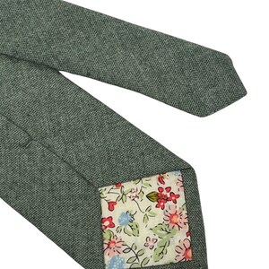 May include: A green patterned tie with a floral print lining. The tie is made of a textured fabric.