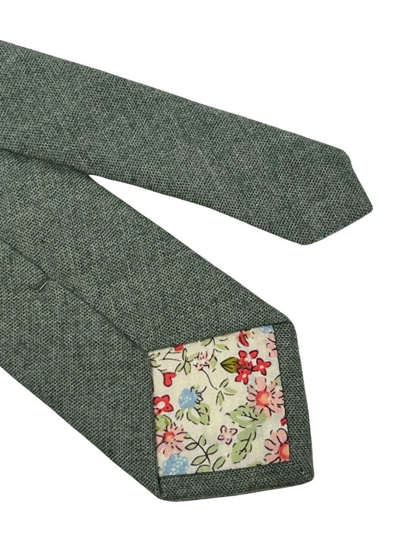 May include: A green patterned tie with a floral print lining. The tie is made of a textured fabric.