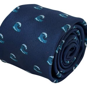 Peut inclure: Une cravate bleu marine foncé ornée d'un motif répétitif de petites vagues stylisées. Les vagues sont représentées dans des tons bleu clair et blanc, illustrant un mouvement de déferlement. Le tissu présente une texture sergée diagonale.