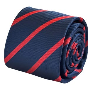 Peut inclure: Cravate roulée bleu marine avec des rayures diagonales rouges audacieuses. La cravate est faite d'un tissu lisse et est bien roulée, mettant en valeur le motif et la texture. Un accessoire classique.