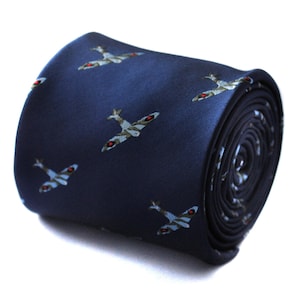 Puede incluir: Corbata enrollada azul marino con un patrón repetido de aviones de combate vintage en gris, blanco y rojo. La corbata está hecha de un material liso, posiblemente seda, y está bien enrollada, mostrando la repetición del patrón.