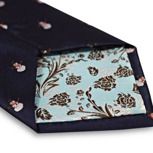 Puede incluir: Una corbata azul marino con un patr&oacute;n de mu&ntilde;eco de nieve blanco. La corbata es reversible y tiene un patr&oacute;n floral azul claro en el otro lado.