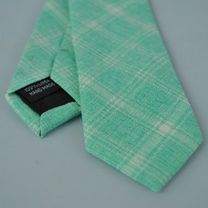 May include: A green and white checkered linen tie with a black label that reads "100% Linen Hand Made".