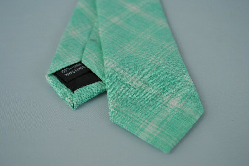 May include: A green and white checkered linen tie with a black label that reads "100% Linen Hand Made".