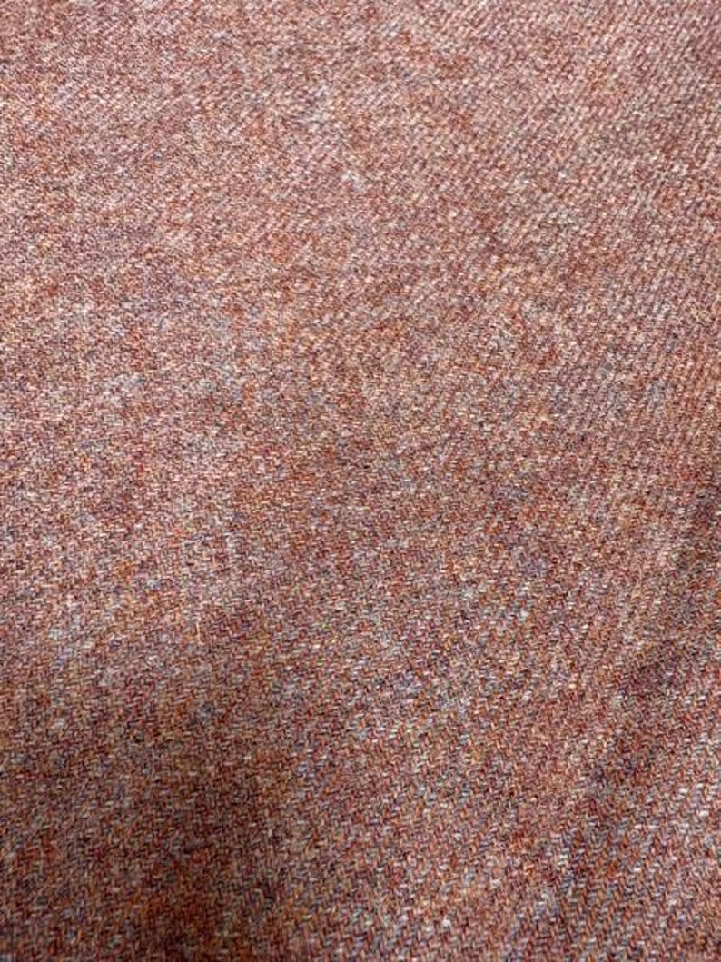 May include: A close-up view of a woven fabric featuring a dense herringbone pattern. The textile displays a blend of earthy tones, including shades of rust, burnt orange, muted brown, and subtle flecks of grey, creating a textured appearance.