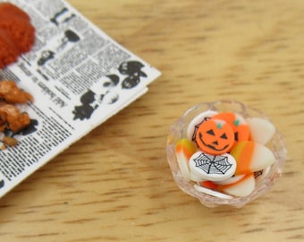 May include: A clear glass bowl filled with Halloween-themed candy. The candy includes orange and white candy corn, orange pumpkin-shaped cookies with black jack-o-lantern faces, and white cookies with black spiderwebs.