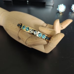 Peut inclure: Un bracelet jonc en or avec une rangée de strass bleus et transparents.