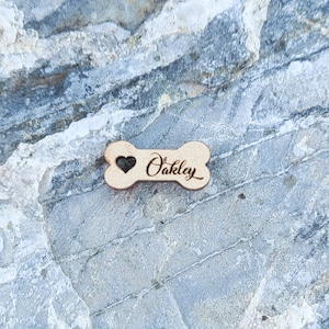 May include: A wooden dog bone tag with a heart and the name "Oakley" engraved on it.