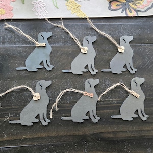 May include: Six metal ornaments shaped like labrador retrievers with a small metal tag attached to each. The tags have different names on them, including "Max", "Duke", and "Mia".