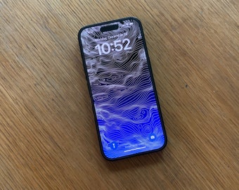 Peut inclure: Un smartphone noir avec un fond d'écran de carte topographique bleu et blanc. Il est 10h52. Le téléphone est sur une surface en bois.