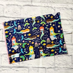 May include: A rectangular fabric pouch with a dark blue background featuring a repeating pattern of mermaids, jellyfish, starfish, and small fish in yellow, green, and orange. A light pink zip runs along the side, and a white label reads bebeco.