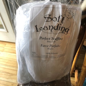 May include: A clear plastic bag filled with white fiber fill. The bag has a label that reads "Soft Landing, Perfect Stuffing, Fiber Fill, Farce Parfaite, Bourre, 100% Polyester." The bag contains 16 oz (1 lb) of stuffing.