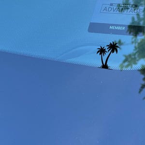 May include: A black silhouette of two palm trees on a blue car windshield with a "Hollywood Kia Advantage Member" sticker in the top right corner.