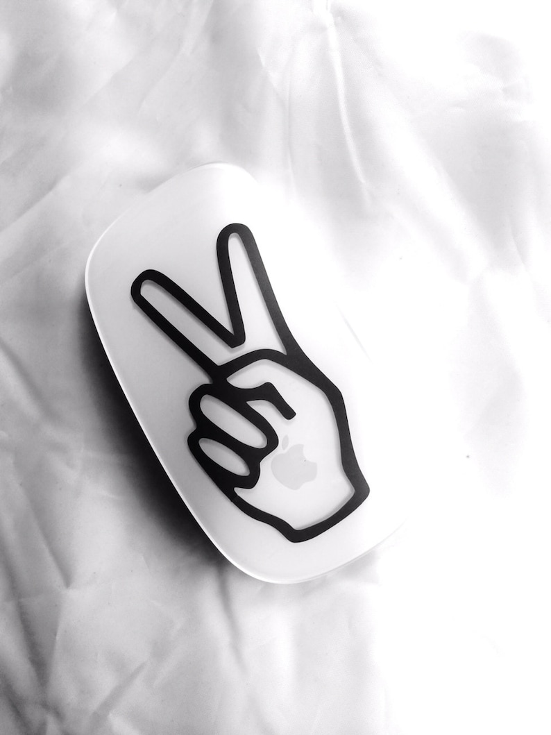 May include: A white wireless mouse with a black peace sign sticker on the top. The peace sign is a hand with two fingers raised in the air.