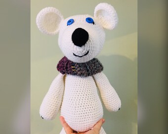 Può includere: Peluche bianco lavorato a uncinetto con occhi a bottone blu e un naso nero. L'animale indossa una sciarpa viola e grigia. Il testo The Burgundy Basket | PHOTOGRID è visibile nella parte inferiore dell'immagine.