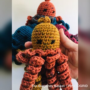 May include: A group of crocheted octopus plushies in various colors, including blue, red, and orange. The octopus in the center is a bright yellow with brown speckles and has a red crocheted body.