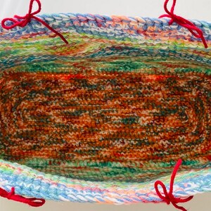 Pu&ograve; includere: Un cesto di uncinetto colorato con manici in filo rosso. Il cesto &egrave; foderato con un tessuto di uncinetto marrone e verde.