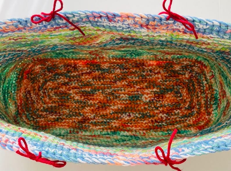 Pu&ograve; includere: Un cesto di uncinetto colorato con manici in filo rosso. Il cesto &egrave; foderato con un tessuto di uncinetto marrone e verde.